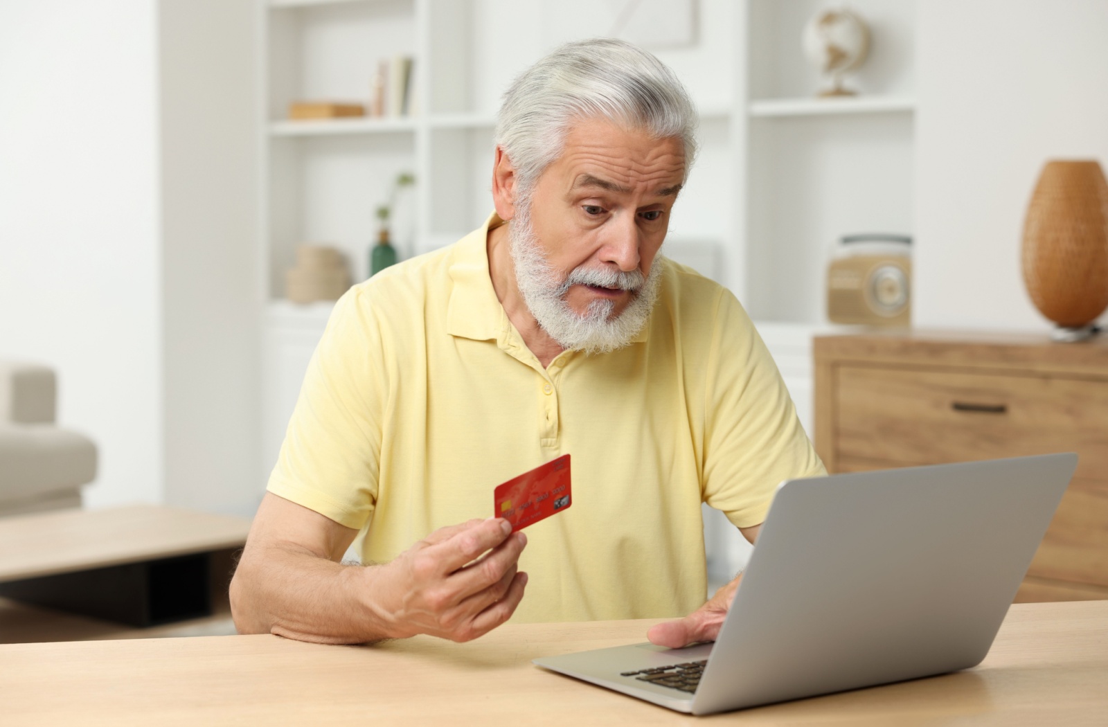 An older adult online holding a credit card in one hand.
