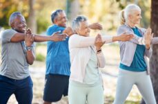 4 seniors standing outdoors in the park smiling and stretching their arms before exercising.