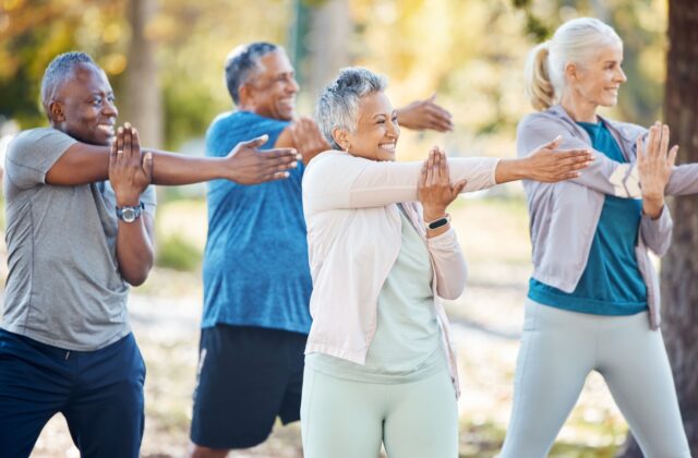 4 seniors standing outdoors in the park smiling and stretching their arms before exercising.