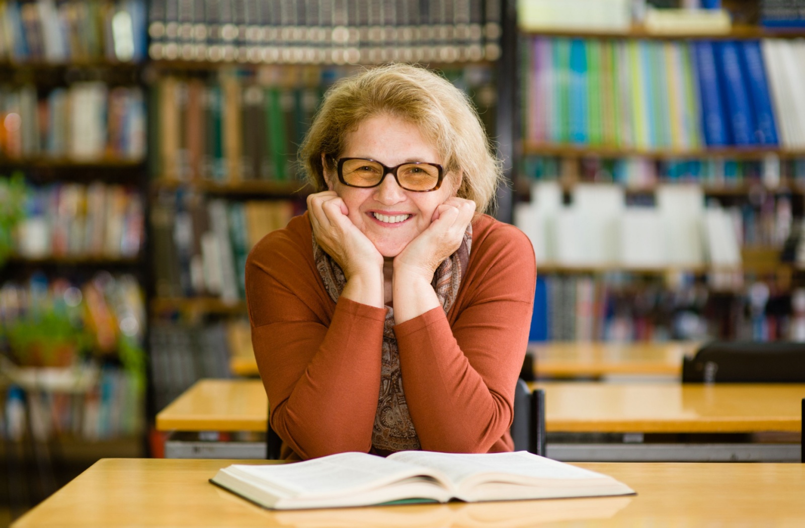 An older adult with an open book smiling while studying and learning in a school library in Rio Rancho.
