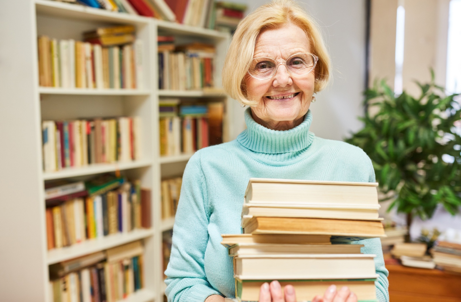 An older adult smiling in the library after picking out a big pile of the best books for seniors.
