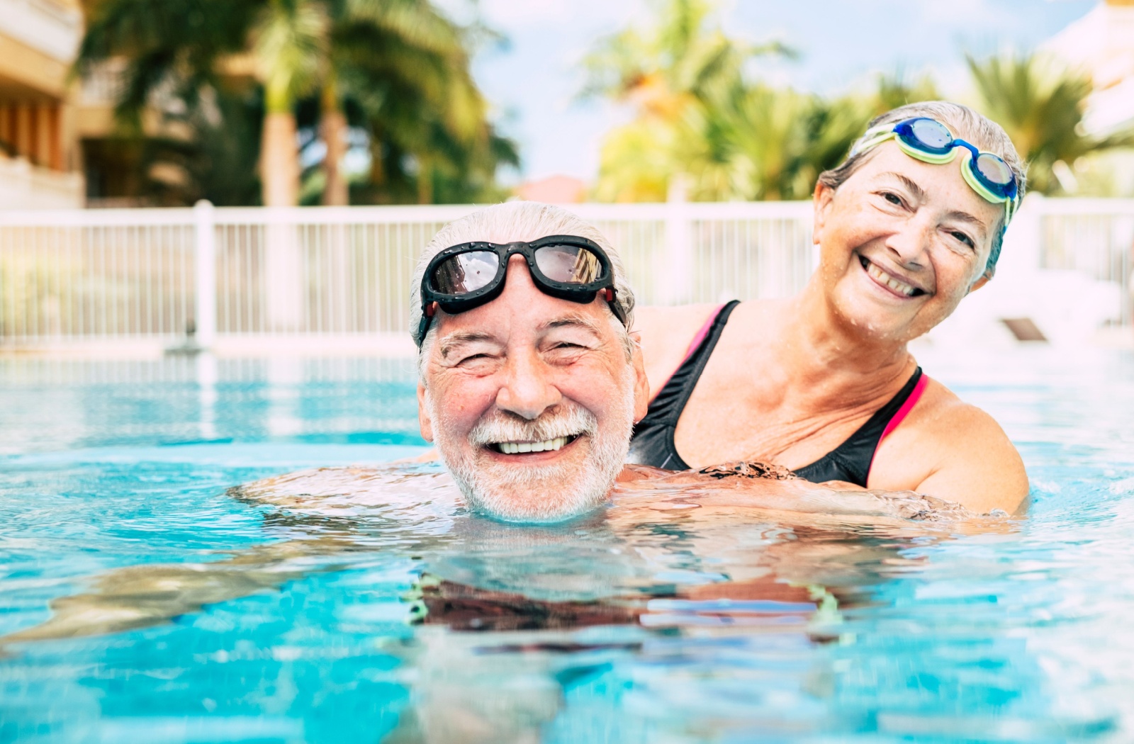 An older couple in the pool smiling and hugging while wearing goggles during swim aerobics.
